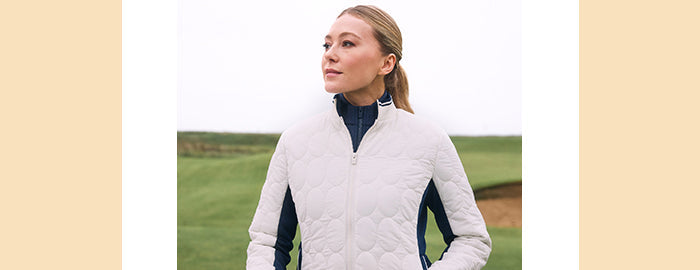 Model on golf course wearing Women's Original Penguin Jersey jacket with quilting in cream with navy panels