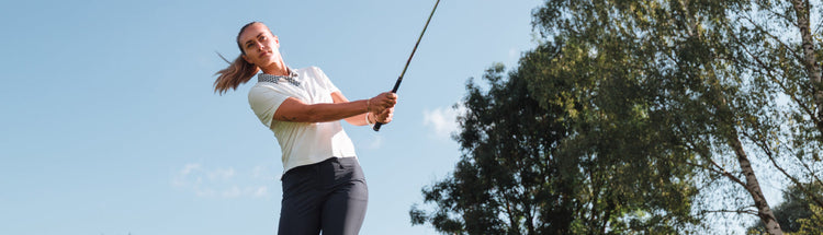 Female golfer completing her drive wearing the new Puma Golf ladies warm white short sleeve polo with navy mosaic print collar.