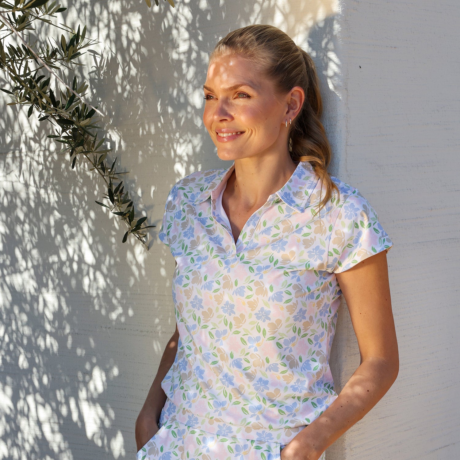 model standing in the shade by a wall, wearing a pastel floral polo from abacus golf