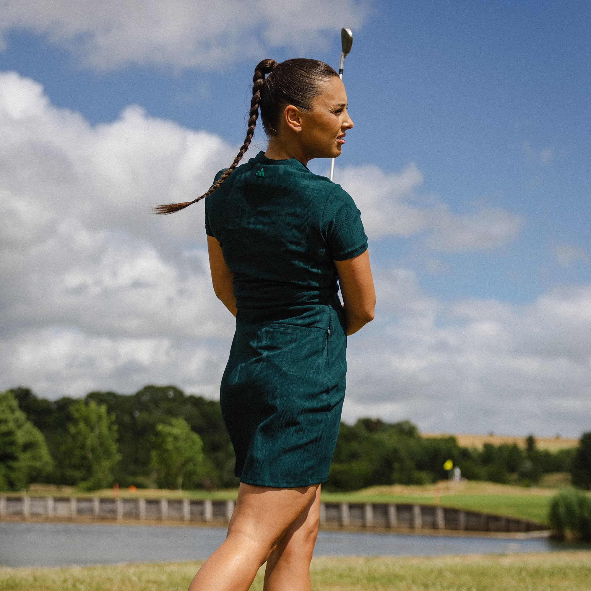 Woman in the adidas golf green short sleeve dress holding a golf club on a golf course