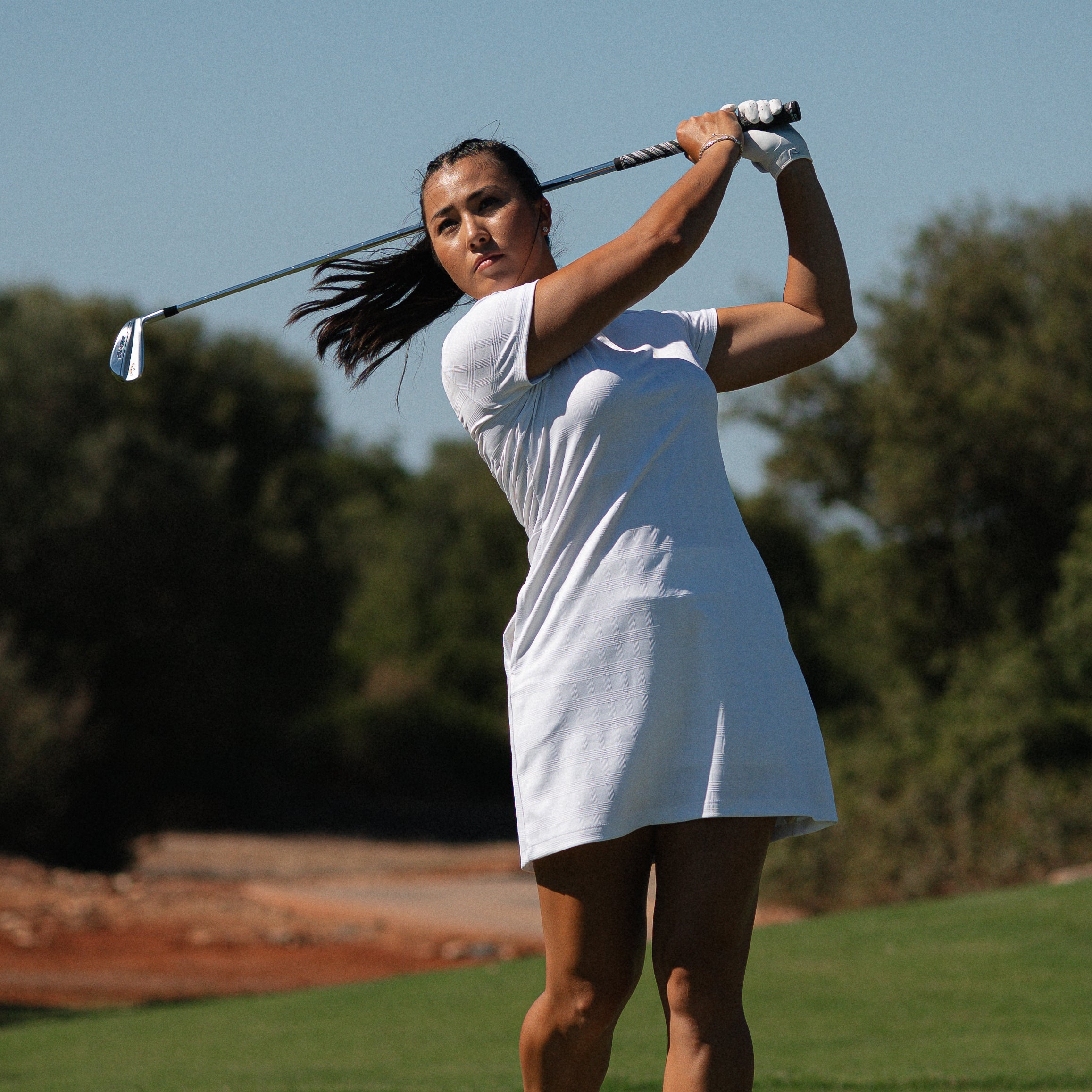 Inci Mehmet completing her swing in the adidas white jacquard finish short sleeve golf dress