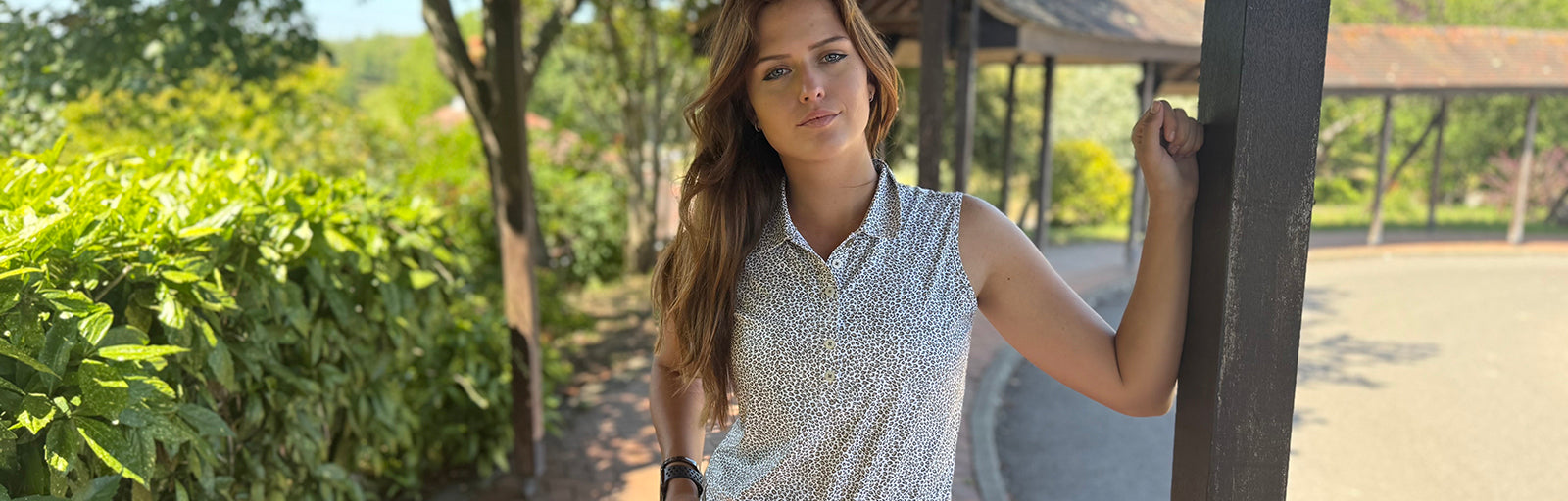 Model wearing Swing out sister golf sleeveless snow leopard animal print polo shirt standing in the shade at a golf club
