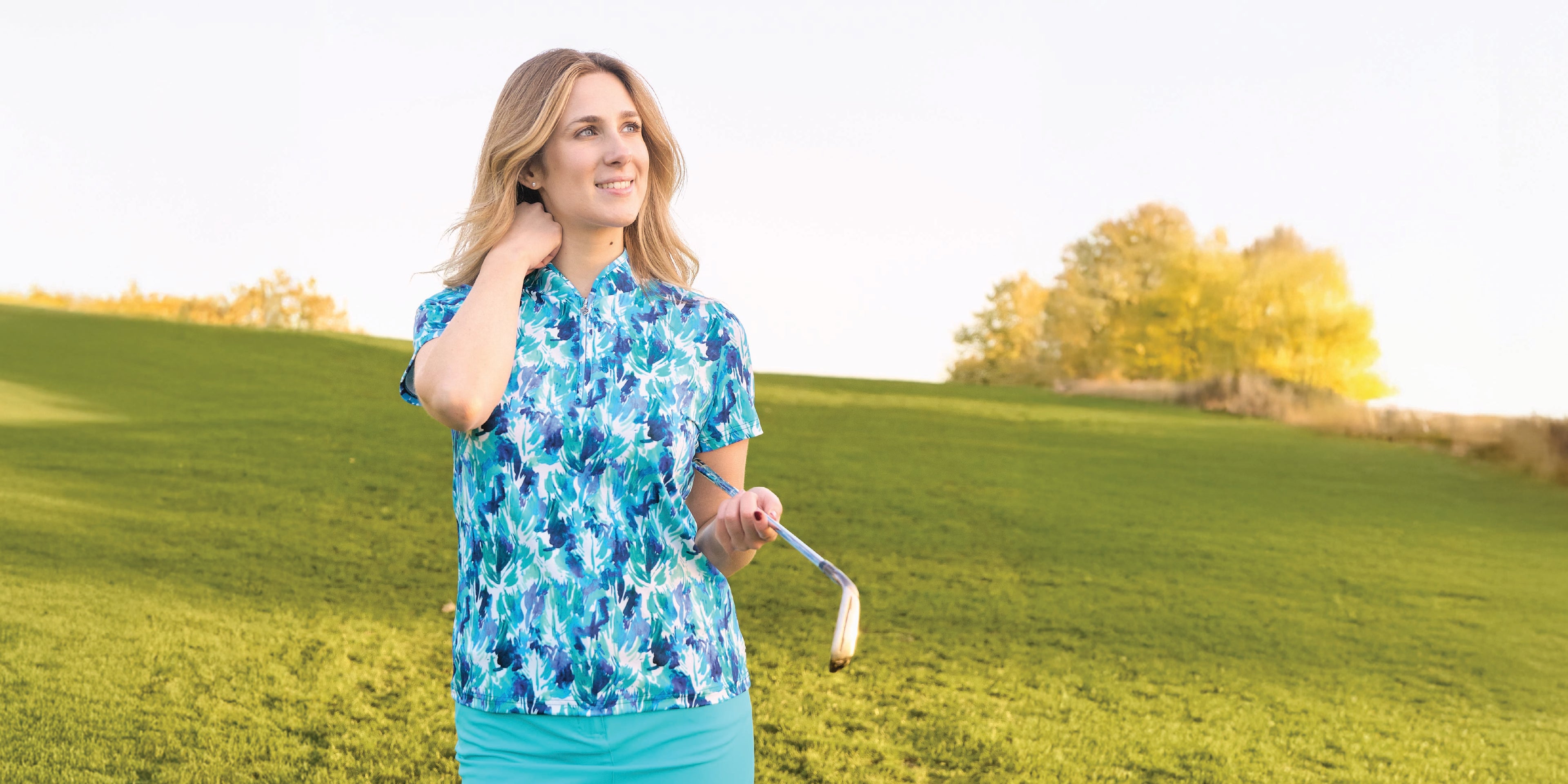 Golfer holding a club under her arm and wearing the Pure Golf Baltic Bliss print short sleeve polo top