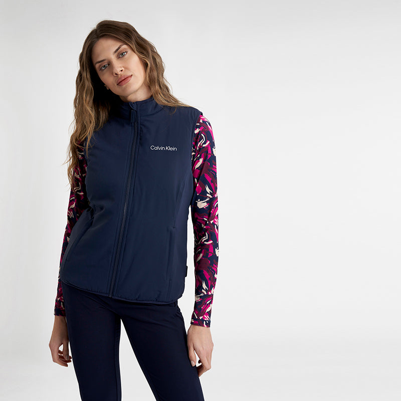 Woman wearing a navy Calvin Klein golf gilet over a brushstroke print in navy burgundy and magenta at GolfGarb