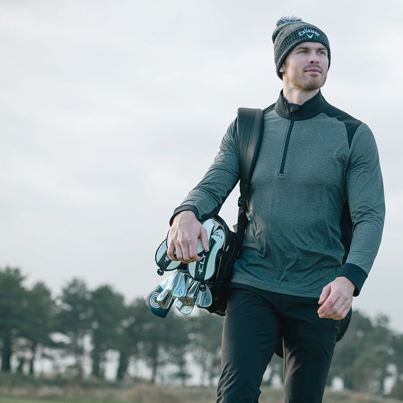 Male golfer with club bag over his shoulder in a Callaway Golf zip neck mid layer top