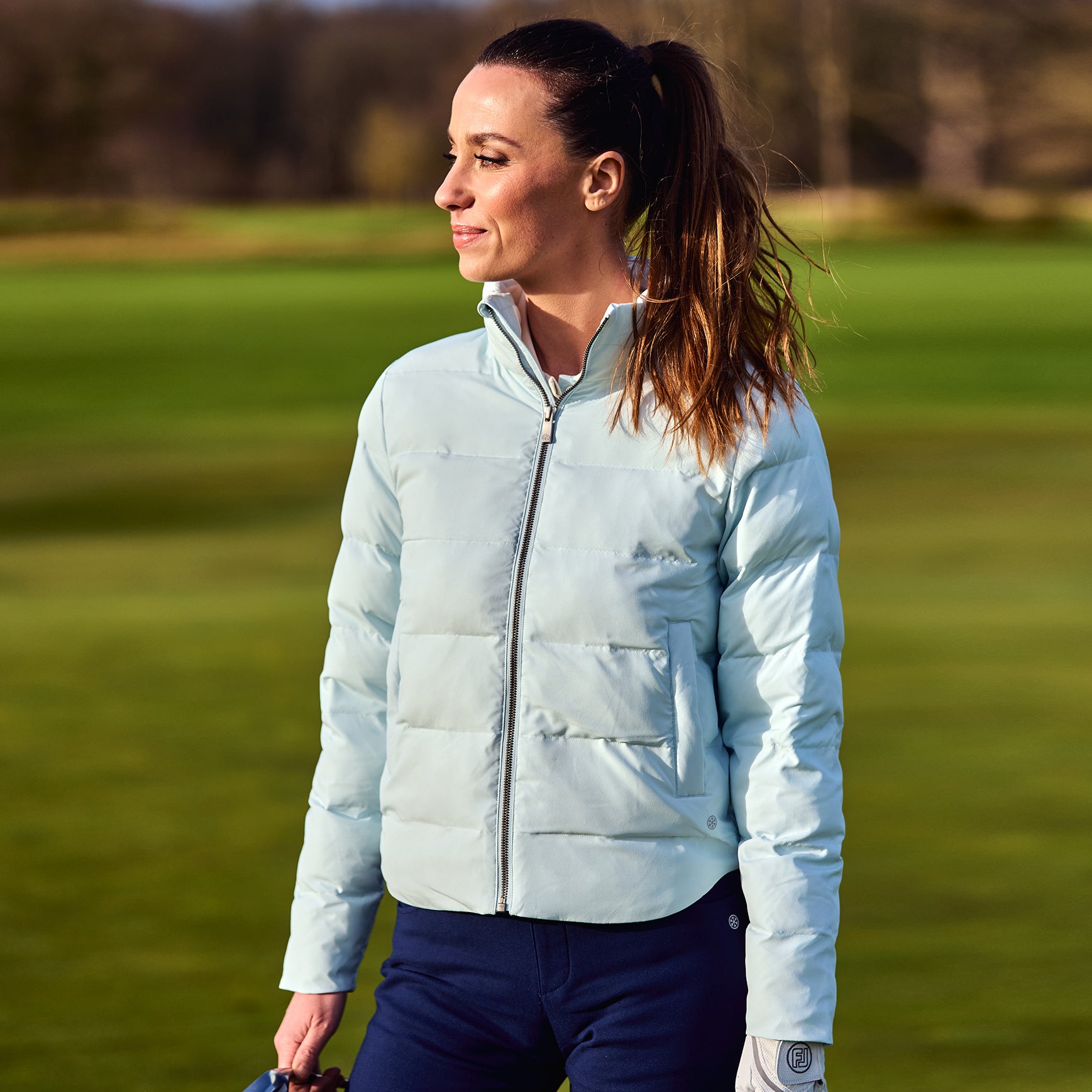 Woman wearing a light blue puffer jacket on a golf course