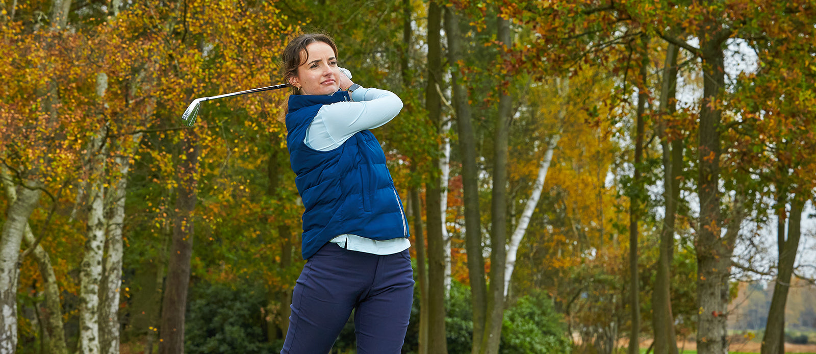 Woman golfer completing her swing in a FootJoy navy gilet and mint long sleeve polo
