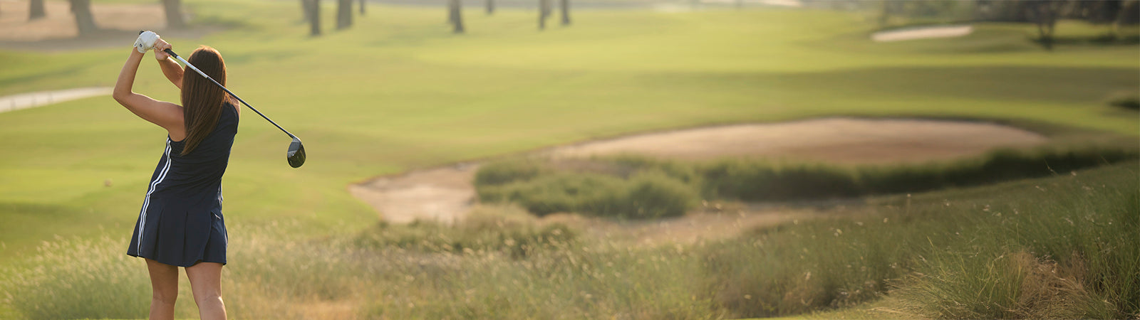 Rear view of a Female golfer completing her shot with a driver wearing a navy blue with white side stripe detail dress from FootJoy