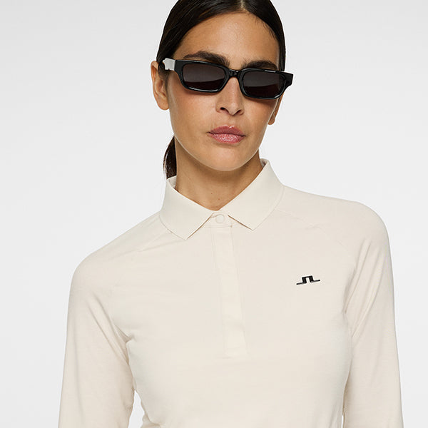 Woman wearing a neutral long sleeve womans golf polo shirt with J.Lindeberg logo.