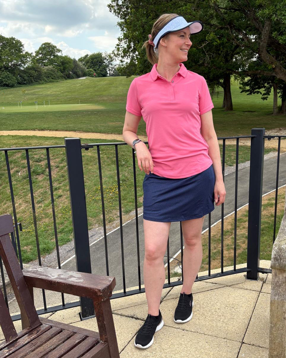 Carolyn wears FootJoy pink polo with fine jacquard stripe in pink lemonade at GolfGarb teamed with the FootJoy navy subtle animal print skort and white and navy animal print visor