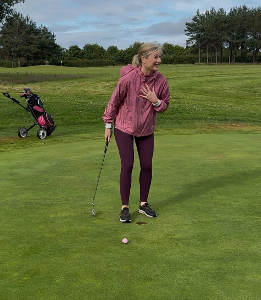 Female new to golf looking happy in disbelief at her shot on a putting green.