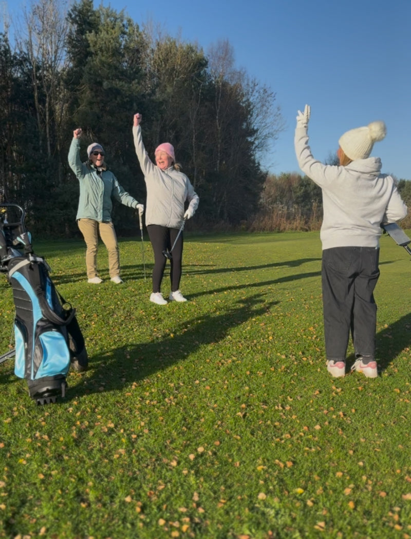 Three female's learning to play golf on a golf course celebrating their shots. 