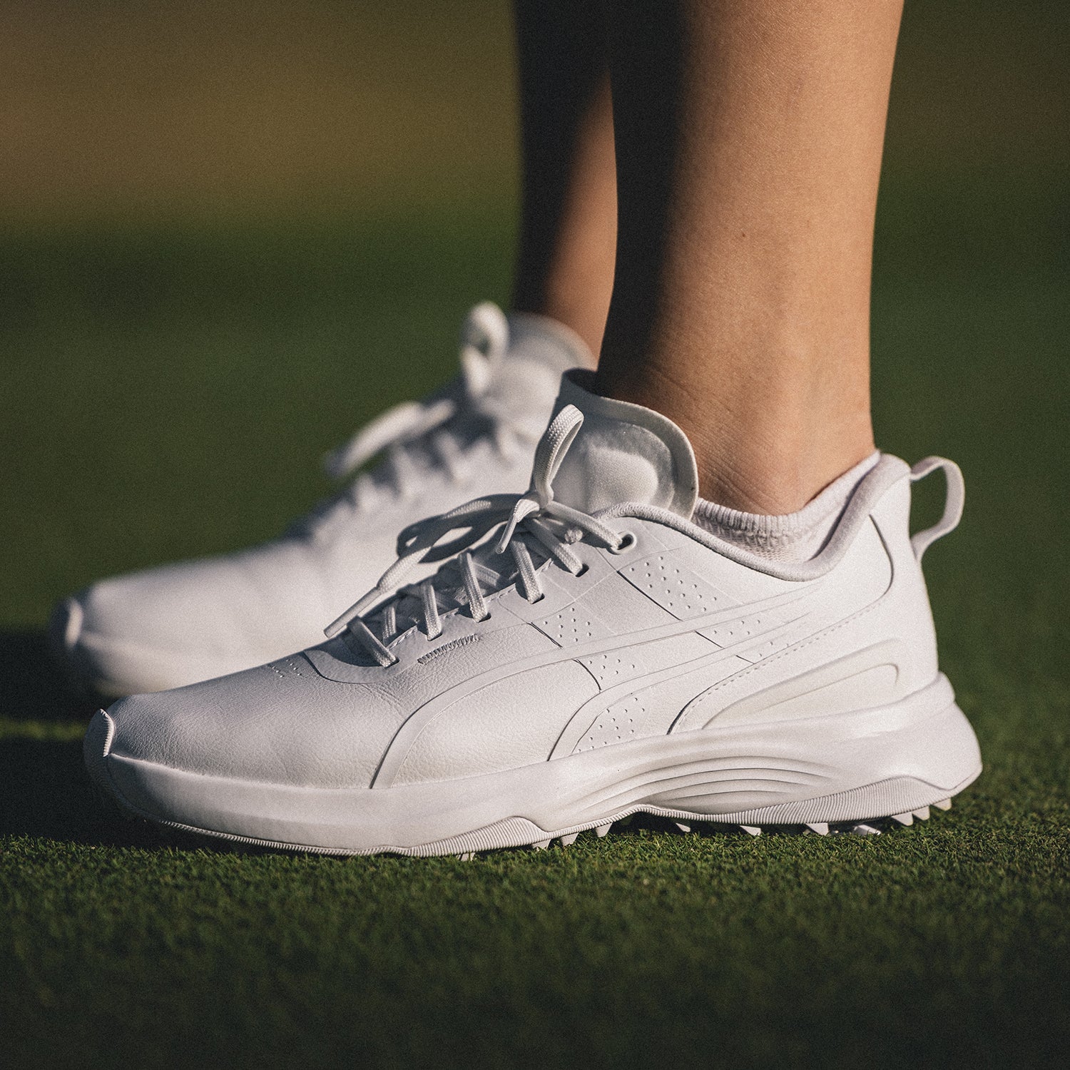 Close up of golfer wearing Puma women's Ignite Blaze waterproof golf shoe in white on a gol green