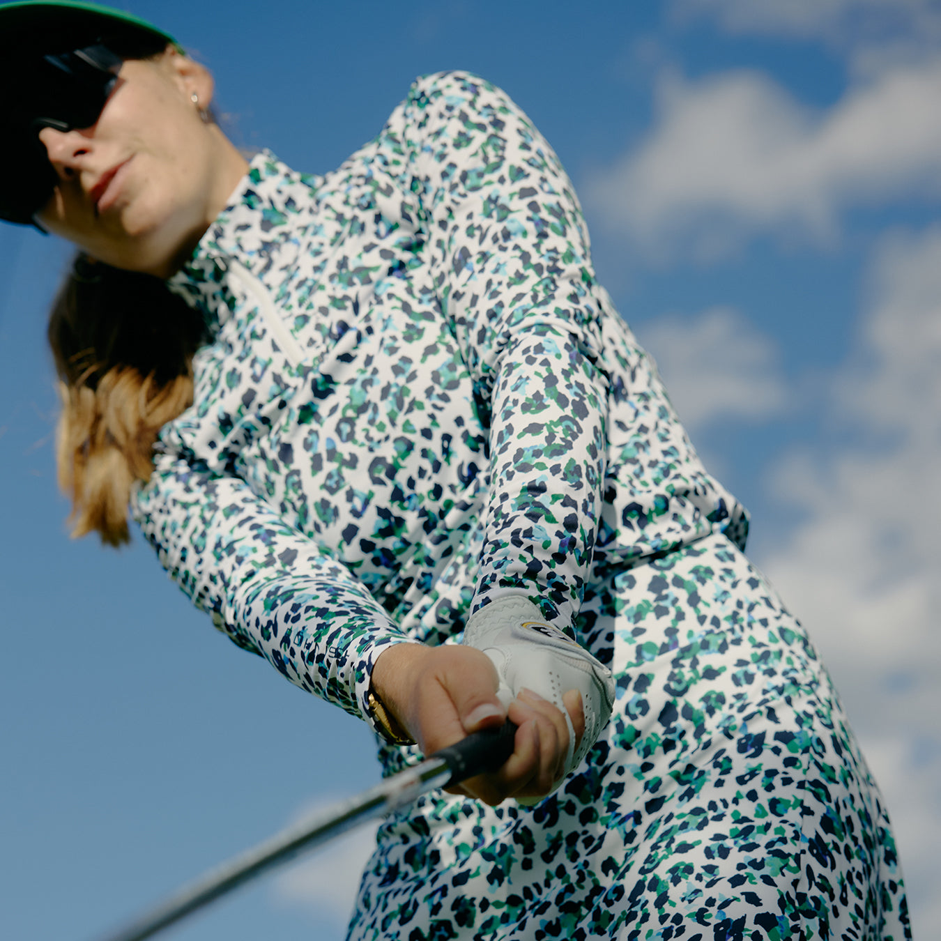 Close up of a female golfer chipping the ball wearing the Rohnisch leo print long sleeve zip neck top and skort in green and navy