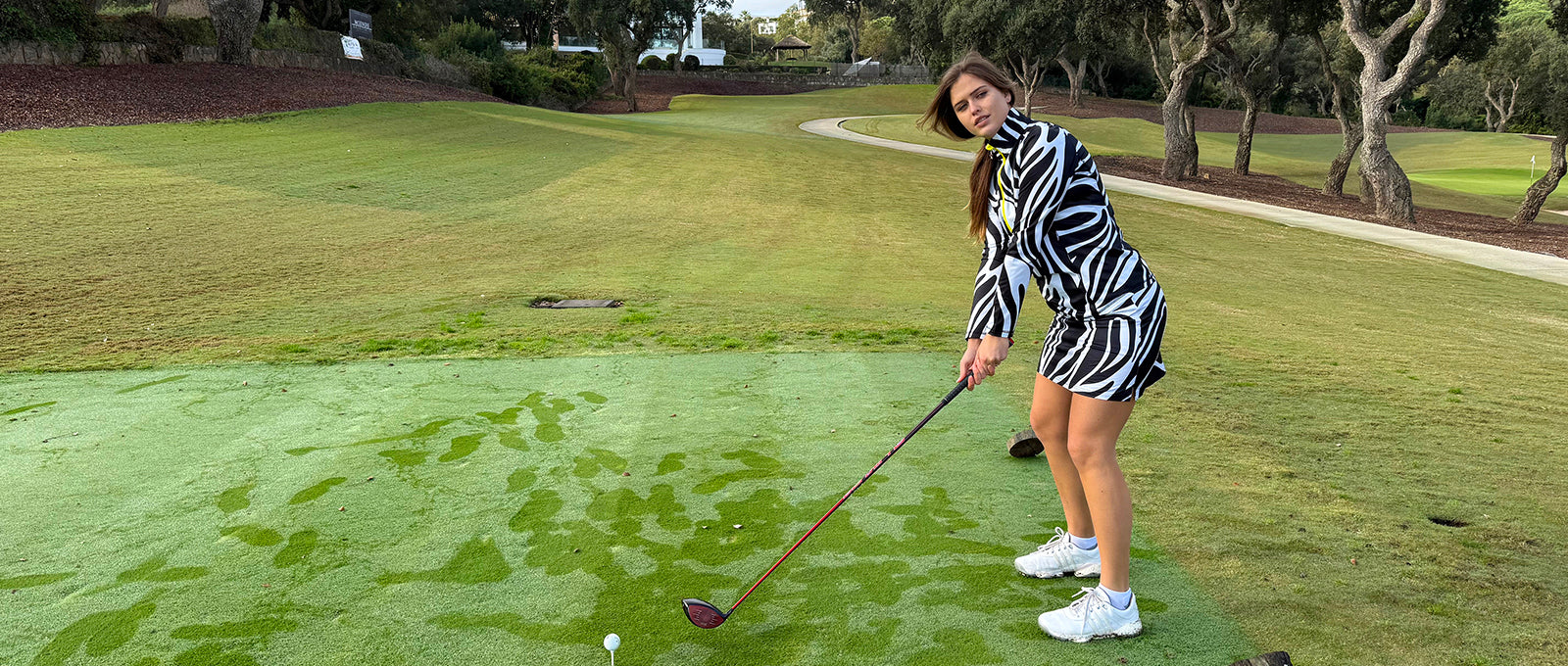 Female golfer wearing Lynx Lime swing out sister golf quarter zip top and skort in black and white zebra print.