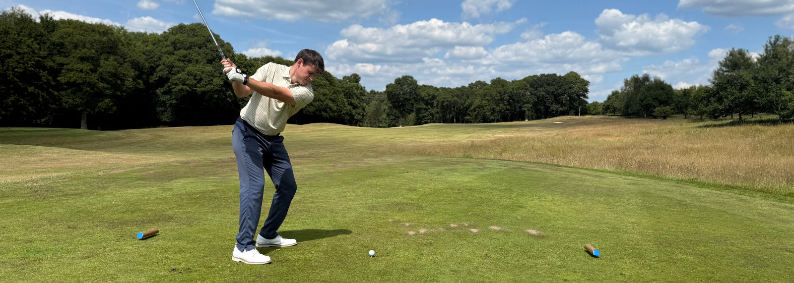 A man in a Swing Out SIster "Brother" golf Polo in soft yellow print tees off on a golf course.