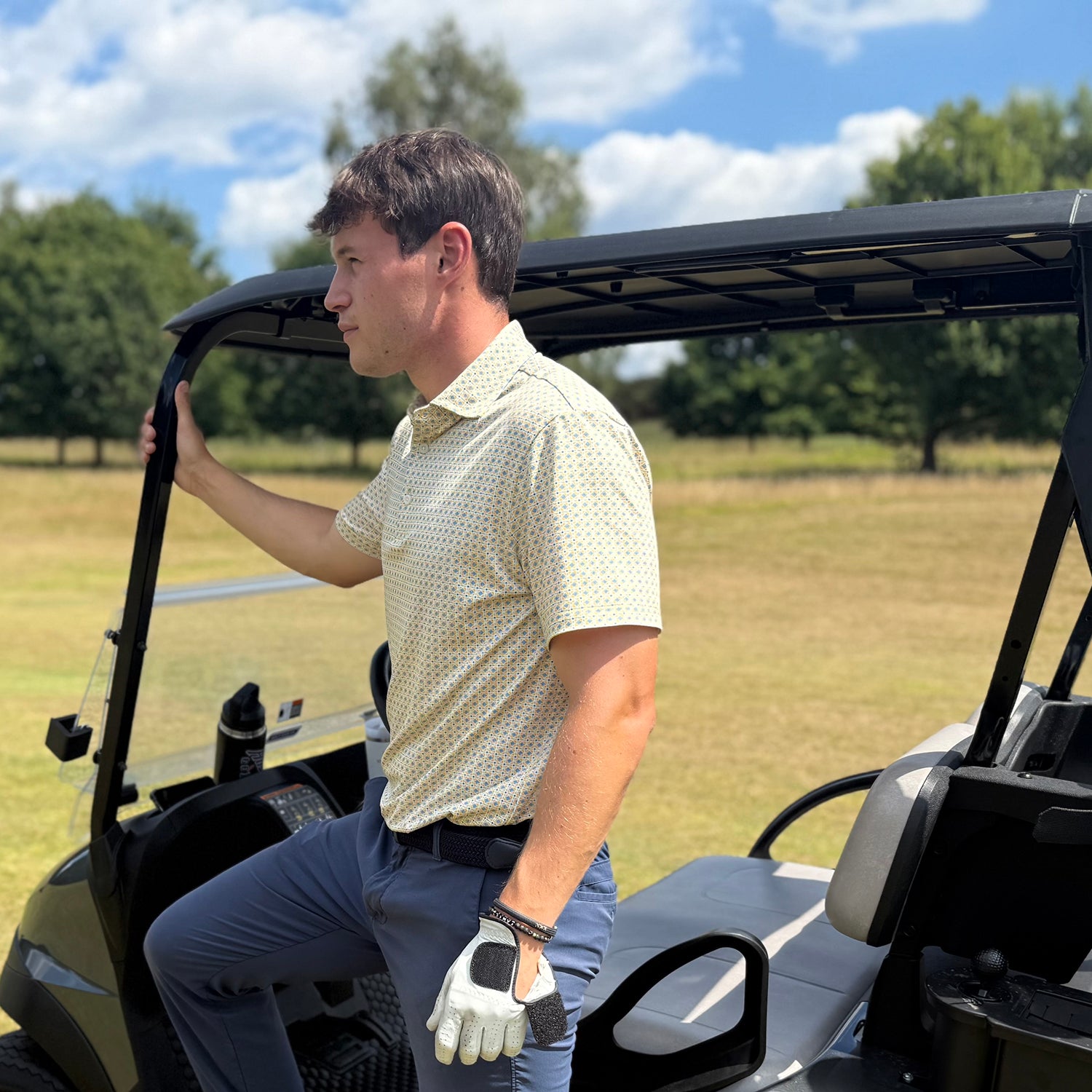 Male golfer standing by his golf cart wearing Swing Out Sister Brother men's soft yellow print short sleeve polo for Breathable Performance & Effortless Movement