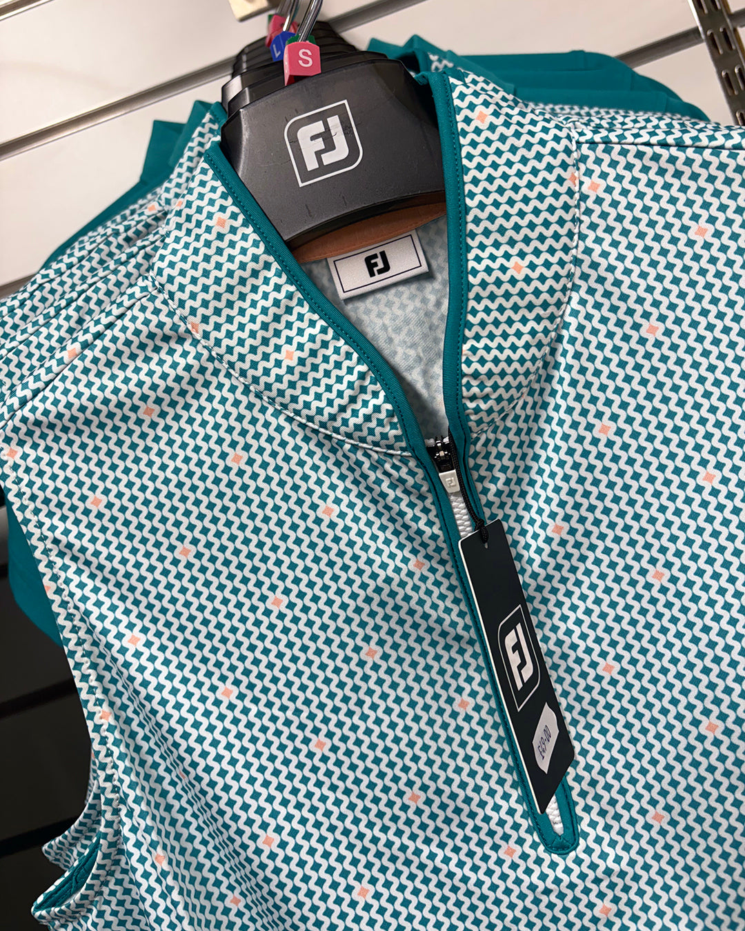 Close up of the FootJoy ladies sleeveless polo in teal geo print on a hanger at Tony Valentine Golf Centre