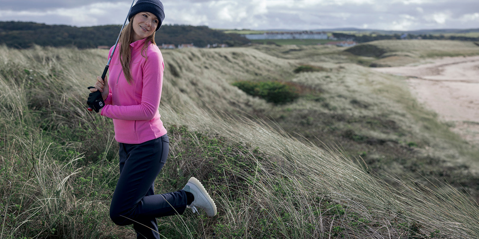 Golfer on the links in Glenmuir women's pink fleece and navy thermal trousers.
