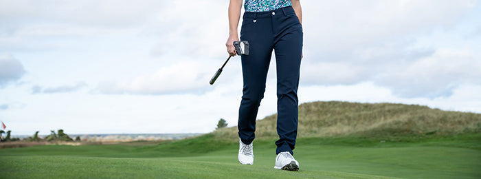 cropped image of a female golfer walking across a course in classic navy golf trousers
