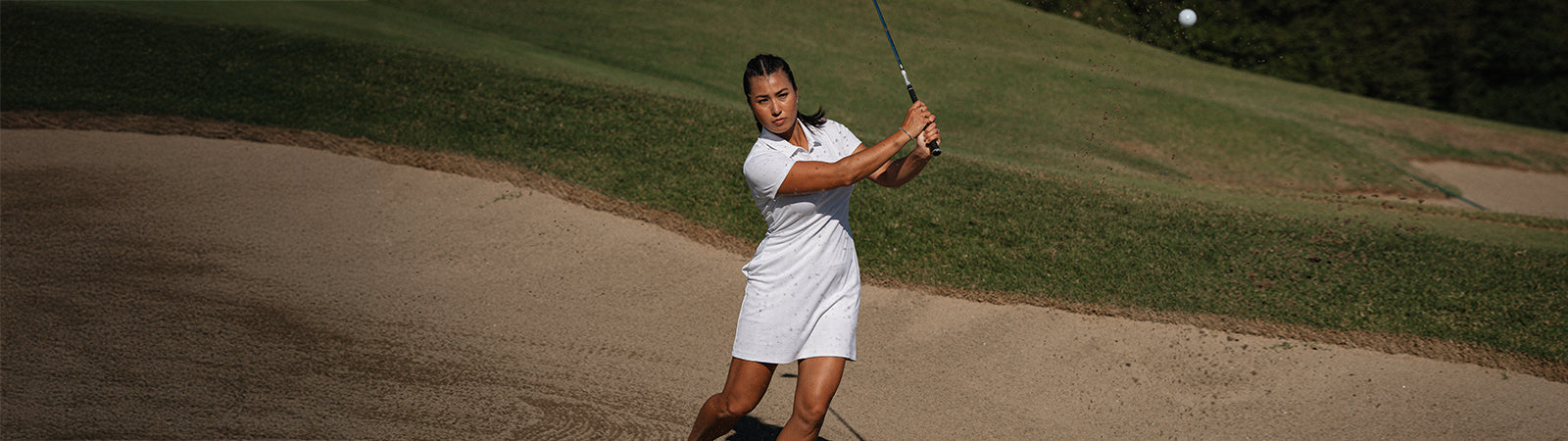 Female pro golfer wearing the adidas short sleeve white golf dress hitting a shot out of the bunker